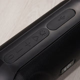 Close-up of the QTX PartyPod Bluetooth speaker's top controls, showing power, volume, light show button and USB port cover above the black mesh grille.