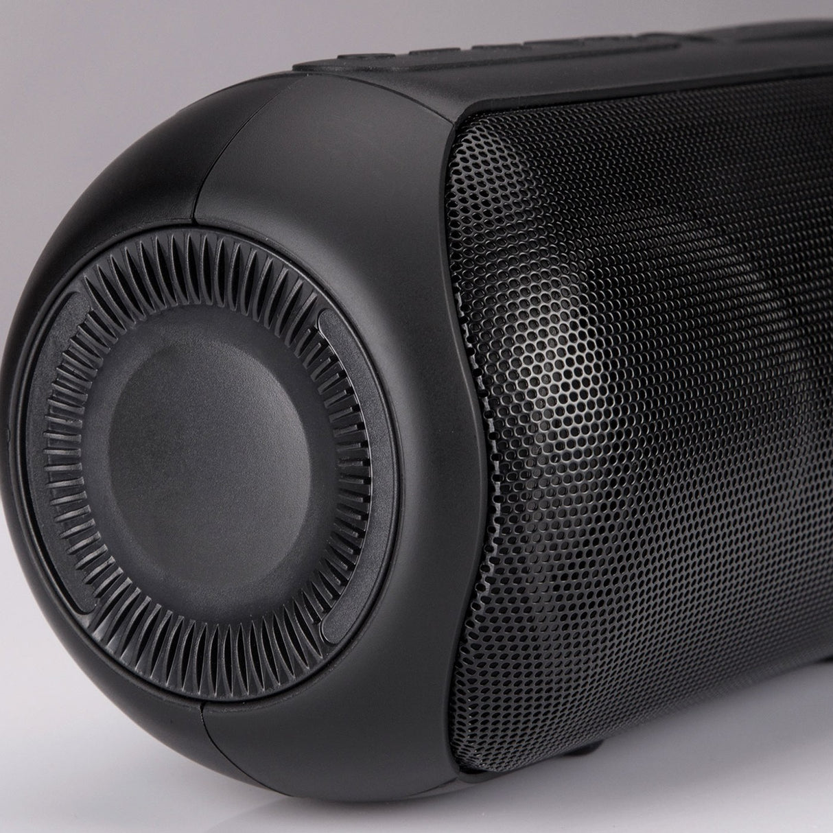 Close-up of the QTX PartyPod Bluetooth speaker by AVSL, showing its matte black cylindrical casing, mesh grille and circular end detail on a light background.