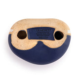 Underside view of the Enjoy the Journey Speckled Ceramic Stone Ornament in blue, showing a sand-speckled base with two eye-like holes and a care label, set against a plain white background.