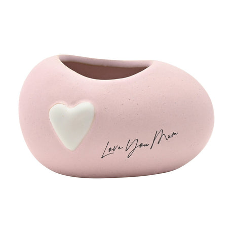 Small pink ceramic planter with a smooth, rounded pebble shape, featuring a raised white heart and 'Love You Mum' script, matte speckled finish, on a plain white background.