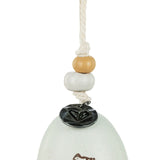 Close-up of a stone-coloured ceramic mini bell ornament's hanging cord with wooden and ceramic beads and a round black charm above the speckled bell top, on a white background.