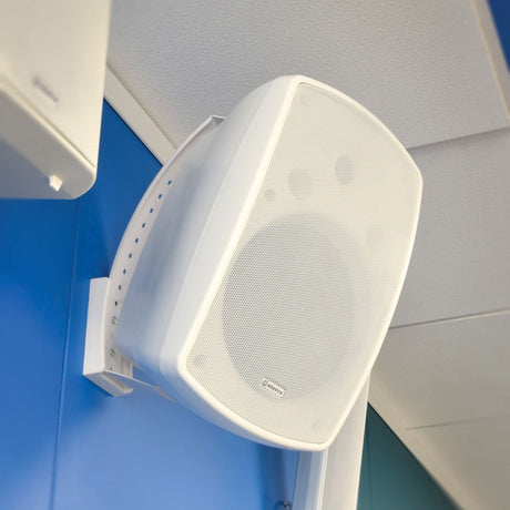 Adastra BH8-W white indoor/outdoor background speaker wall-mounted on a blue panel with pan and tilt bracket, shown angled downward near the ceiling.