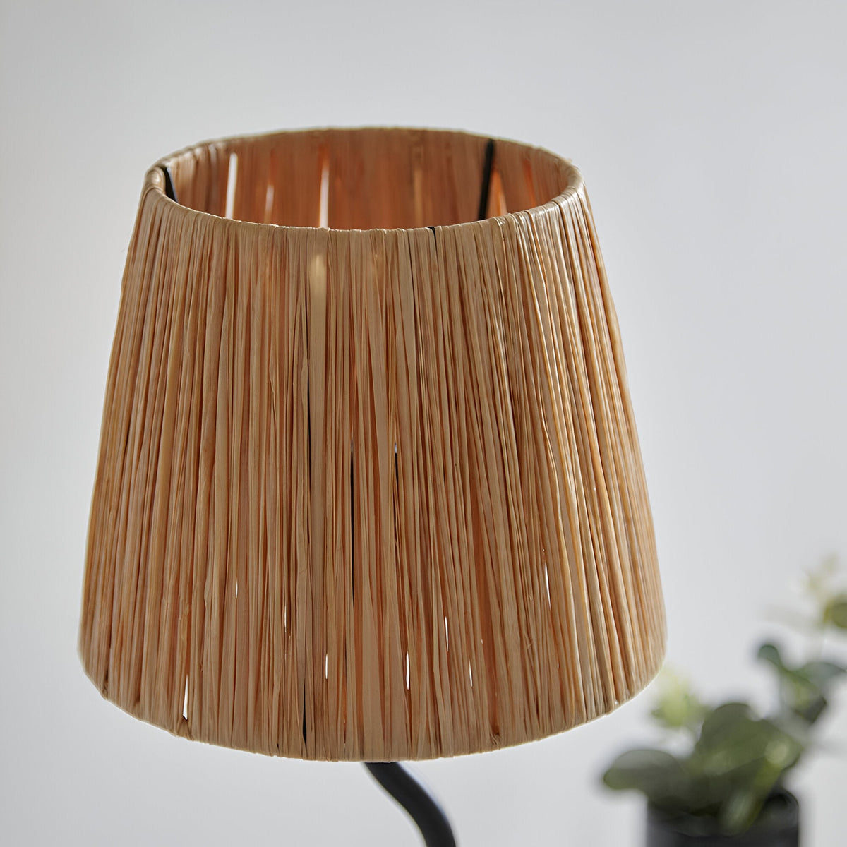 Endon Danemont table lamp close-up showing the tapered hand-wrapped natural raffia shade on a slim matt black metal frame against a pale wall.