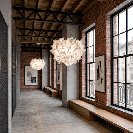 A modern industrial hallway with exposed brick, large windows, wooden benches, and concrete floors features two Violla 2 Light Pendant - White fixtures overhead, while framed abstract art adds character to the space.