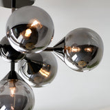 Endon Fitzroy 6 light semi-flush ceiling light in black chrome, close-up of smoked glass globes clustered around brass arms with lit G9 lamps.