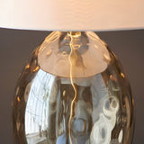 Close-up of the Endon Draycott dimpled glass table lamp base in satin brass with a vintage white fabric drum shade glowing softly above.