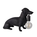 Bevworth Table Lamp in matt black resin, shaped as a seated dachshund holding an E27 filament bulb in its mouth, on a plain white background.