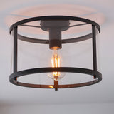 Endon Ellery flush ceiling light in black with a cylindrical clear glass shade and exposed E27 filament bulb, mounted to a white ceiling.