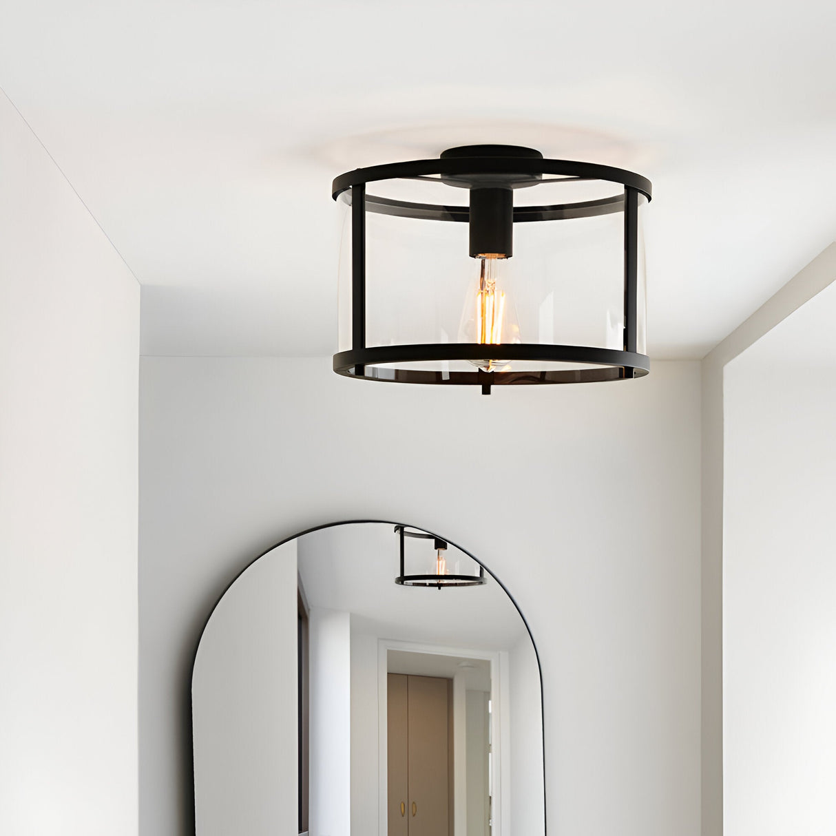 Endon Ellery flush ceiling light in black with a cylindrical glass shade and E27 filament bulb, installed in a hallway above an arched mirror.