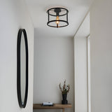 Endon Ellery black flush ceiling light with cylindrical open cage frame and glass shade, installed in a hallway above a console table and round black mirror.
