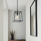Brenton Lantern Pendant in black, a tapered box-frame ceiling light with clear glass panels and visible filament bulb, hung from a chain in a hallway.