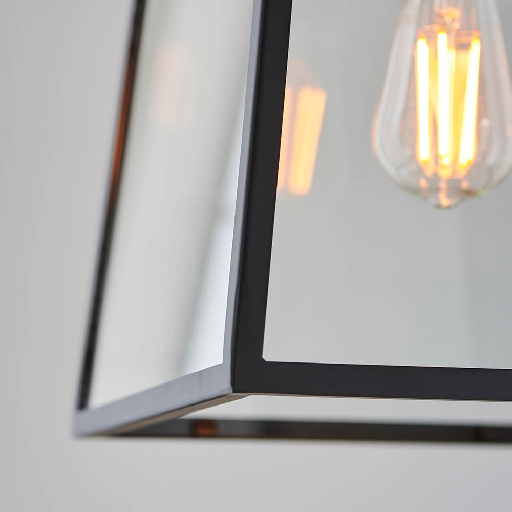 Close-up of the Brenton Lantern Pendant in black, showing tapered metal frame corners with clear glass panels and a visible filament bulb.