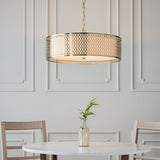 Rosaline 3 Light Pendant in gold with circular fretwork outer and white fabric inner shade, hung above a marble dining table in a panelled room.