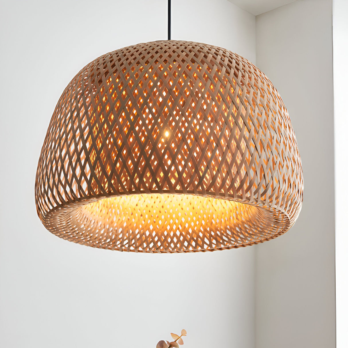 Aldstead Oval Pendant in natural woven rattan with a domed shade and warm interior glow, shown against a white wall in a bright room.