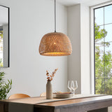 Aldstead Oval Pendant in natural rattan weave with black metal fitting, hung above a dining table in a bright kitchen setting.