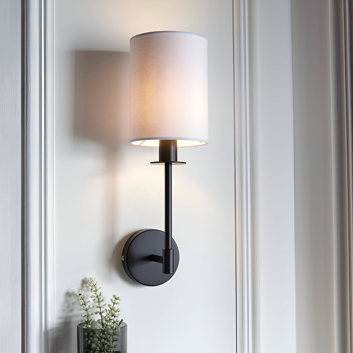 Endon Cliffhurst wall light with a slim matt black upright and round backplate topped by a vintage white cylinder shade, mounted on a panelled wall.