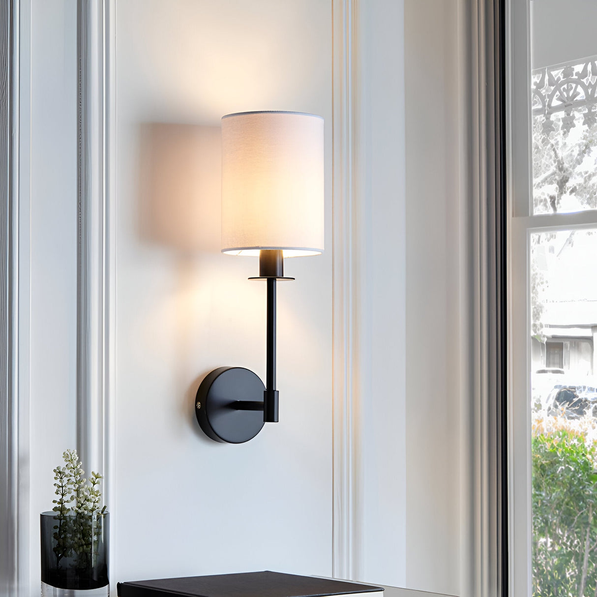 Endon Cliffhurst wall light with slim matt black upright and vintage white cylinder shade, mounted between windows in a bright living space.