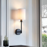Endon Cliffhurst wall light with slim matt black upright and vintage white cylinder shade, mounted between windows in a bright living space.