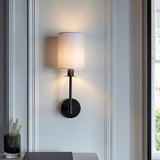 Endon Cliffhurst wall light with a slim matt black upright and vintage white cylinder shade, mounted beside a window above a console with a vase.