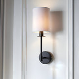 Endon Cliffhurst wall light with a slim matt black upright and round backplate topped by a vintage white cylinder shade, mounted on a panelled wall.