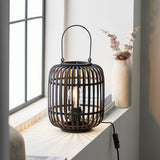 Endon Bracken table lamp in black with an open bamboo cage, arched handle and E27 filament bulb, lit on a windowsill beside a vase of eucalyptus.