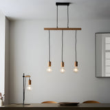 Cranbury 3-Light Linear Pendant in black and natural wood with staggered exposed filament bulbs, shown above a dining table beside a matching table lamp.