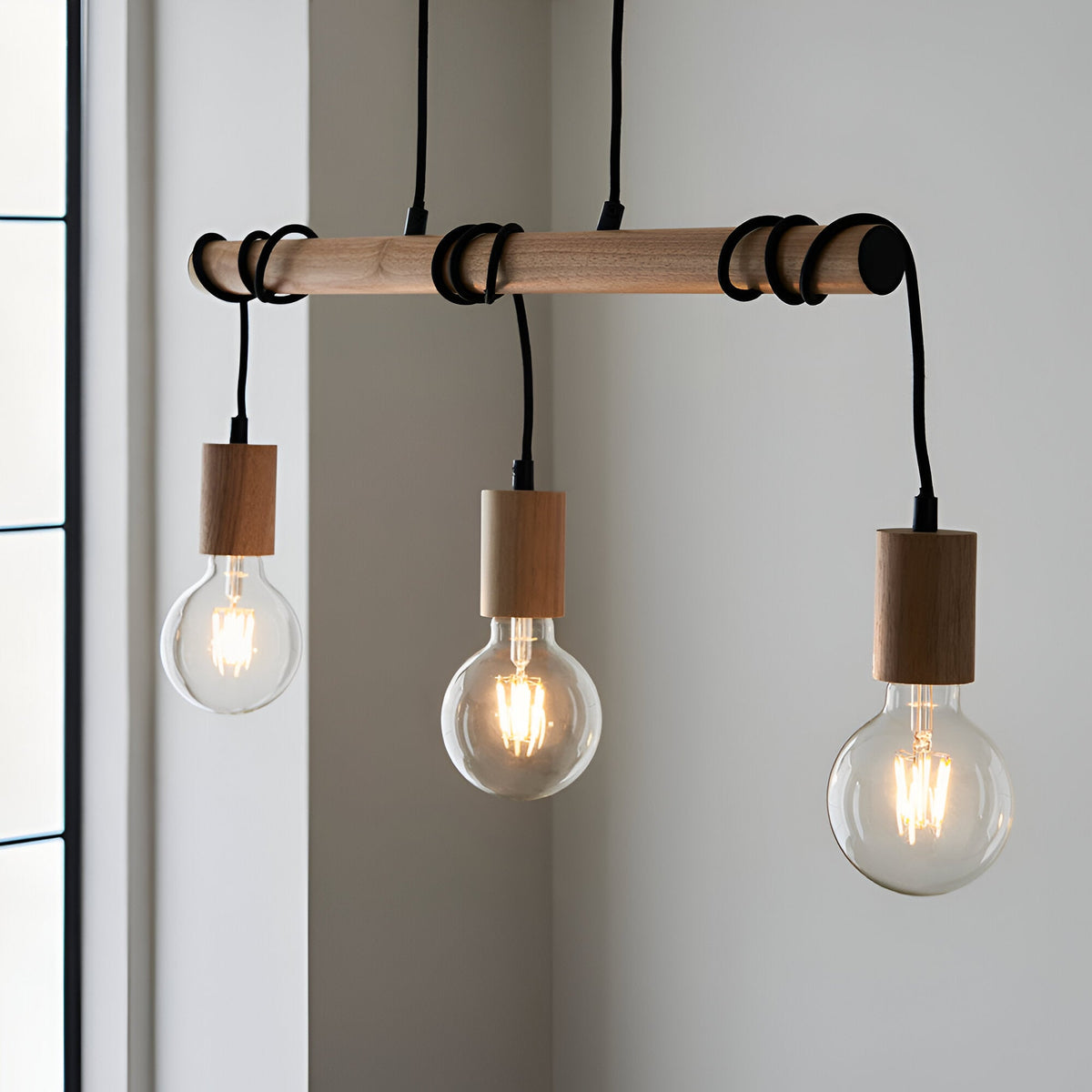 Cranbury 3 Light Linear Pendant in black and natural wood, three exposed filament bulbs hanging from a wooden bar, shown against a light grey wall.