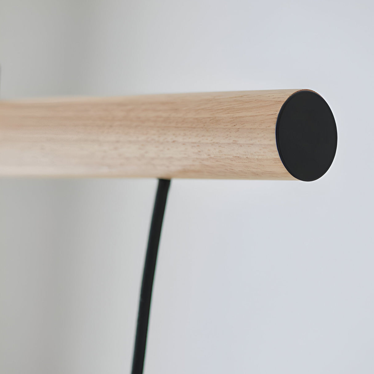Close-up of the Cranbury 3 Light Linear Pendant's end cap, showing natural wood arm with matt black circular fitting and cable, on a plain white background.