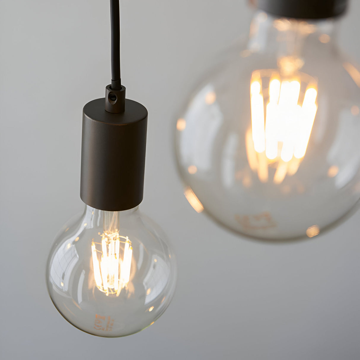 Close-up of Endon Cliffwell pendant with anthracite lampholder, black flex and two exposed E27 globe filament bulbs glowing on a light grey background.
