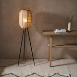 Daneshaw Floor Lamp with woven natural linen shade on a bamboo frame and black tripod base, glowing beside a wooden console table.