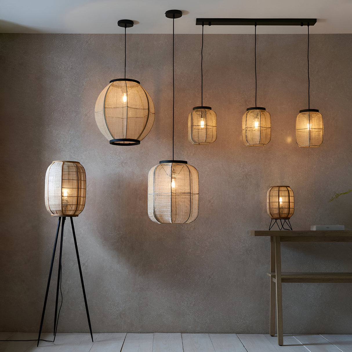 Daneshaw Floor Lamp with natural linen drum shade on bamboo frame and matt black tripod base, shown lit among pendant lights in a room setting.