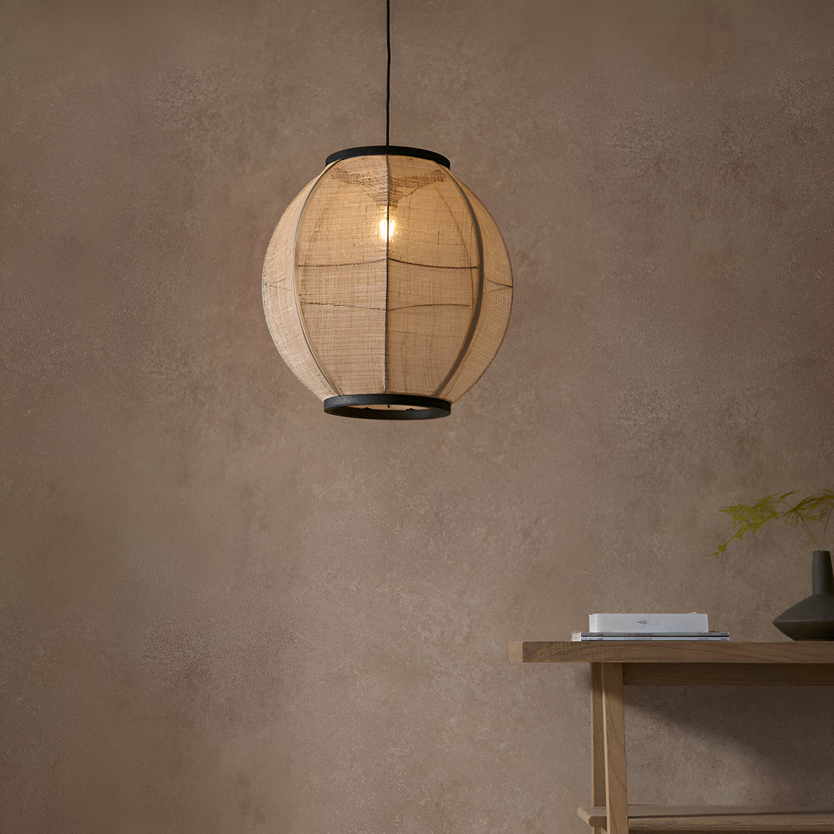 Daneshaw Pendant Light in black and natural linen, spherical shade with matt black trim rings, hanging lit above a wooden console table.