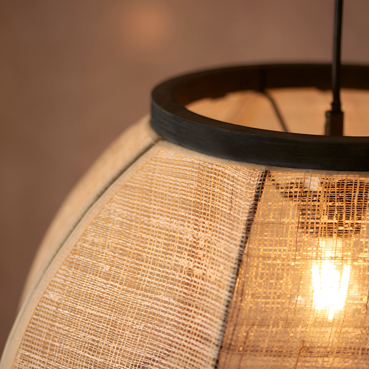 Close-up of the Daneshaw pendant light showing woven natural linen shade with matt black metal ring trim and lit E27 bulb inside.