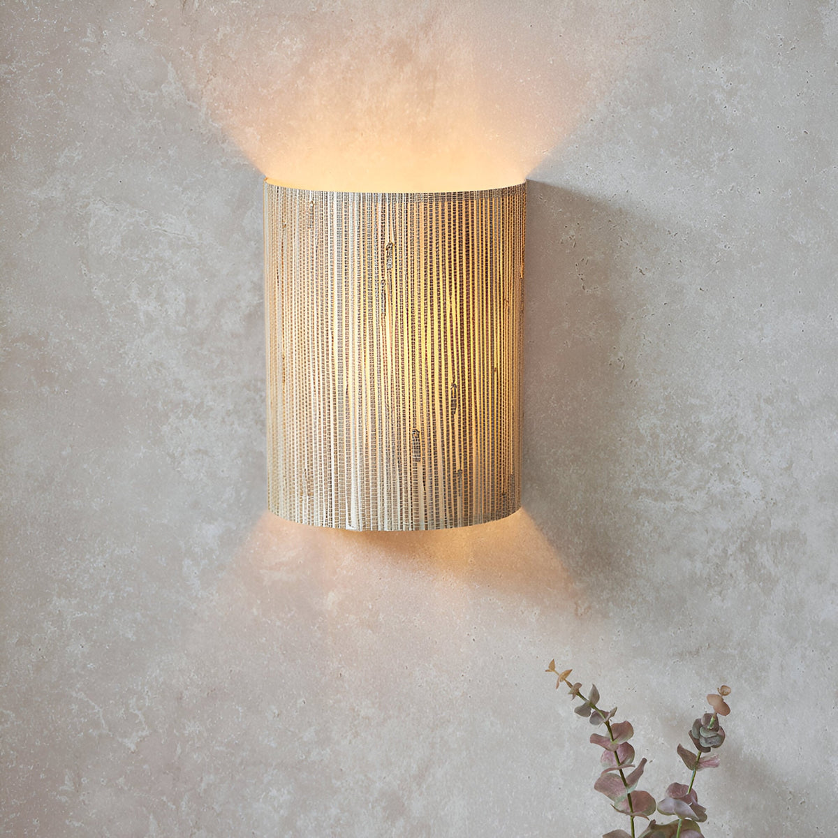 Endon Salcombe wall light with woven natural seagrass half-cylinder shade casting a warm up and down glow on a light plaster wall.