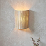 Endon Salcombe wall light with woven natural seagrass half-cylinder shade casting a warm up and down glow on a light plaster wall.