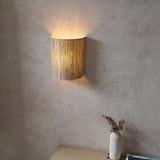 Endon Salcombe wall light with woven natural seagrass half-cylinder shade casting a warm glow on a textured plaster wall above a wooden console.