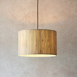 Salcombe Pendant Light in black and natural, a drum-shaped fixture with woven seagrass shade on a black cable, shown lit against a plain neutral wall.