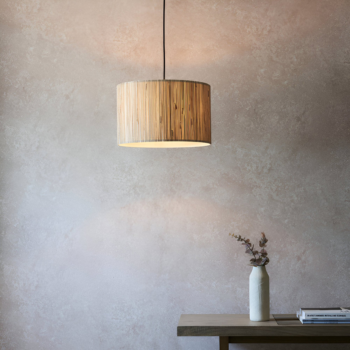 Salcombe Pendant Light with woven natural seagrass drum shade and black cable, hanging above a console table in a neutral-toned room.