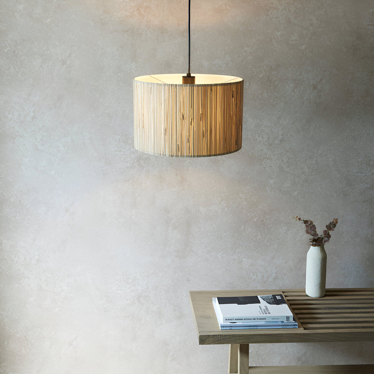 Salcombe Pendant Light in black and natural woven seagrass drum shade, hung on black cable above a wooden table in a neutral room setting.