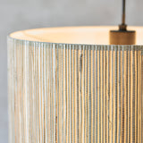 Close-up of the Salcombe Pendant Light's woven natural seagrass drum shade with matt black metal fittings and cable, set against a plain grey background.