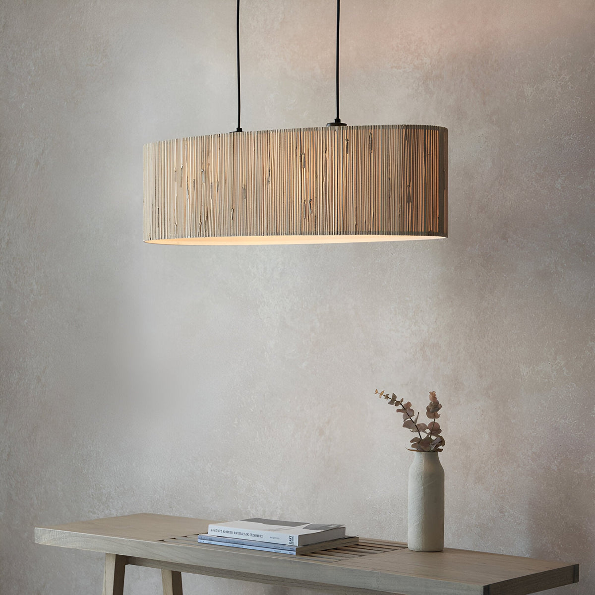 Endon Salcombe 2 light linear pendant with woven natural seagrass oval shade and matt black cables, hung above a wooden console with a vase.