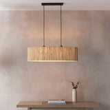 Endon Salcombe 2 light linear pendant with woven natural seagrass oval shade and matt black cables, hanging above a wooden console against a warm pink wall.