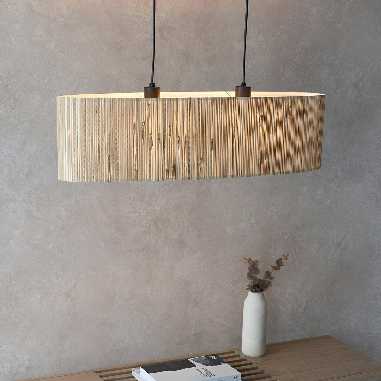 Endon Salcombe 2 light linear pendant with woven natural seagrass oval shade and matt black cables, lit above a wooden console with a vase of eucalyptus.