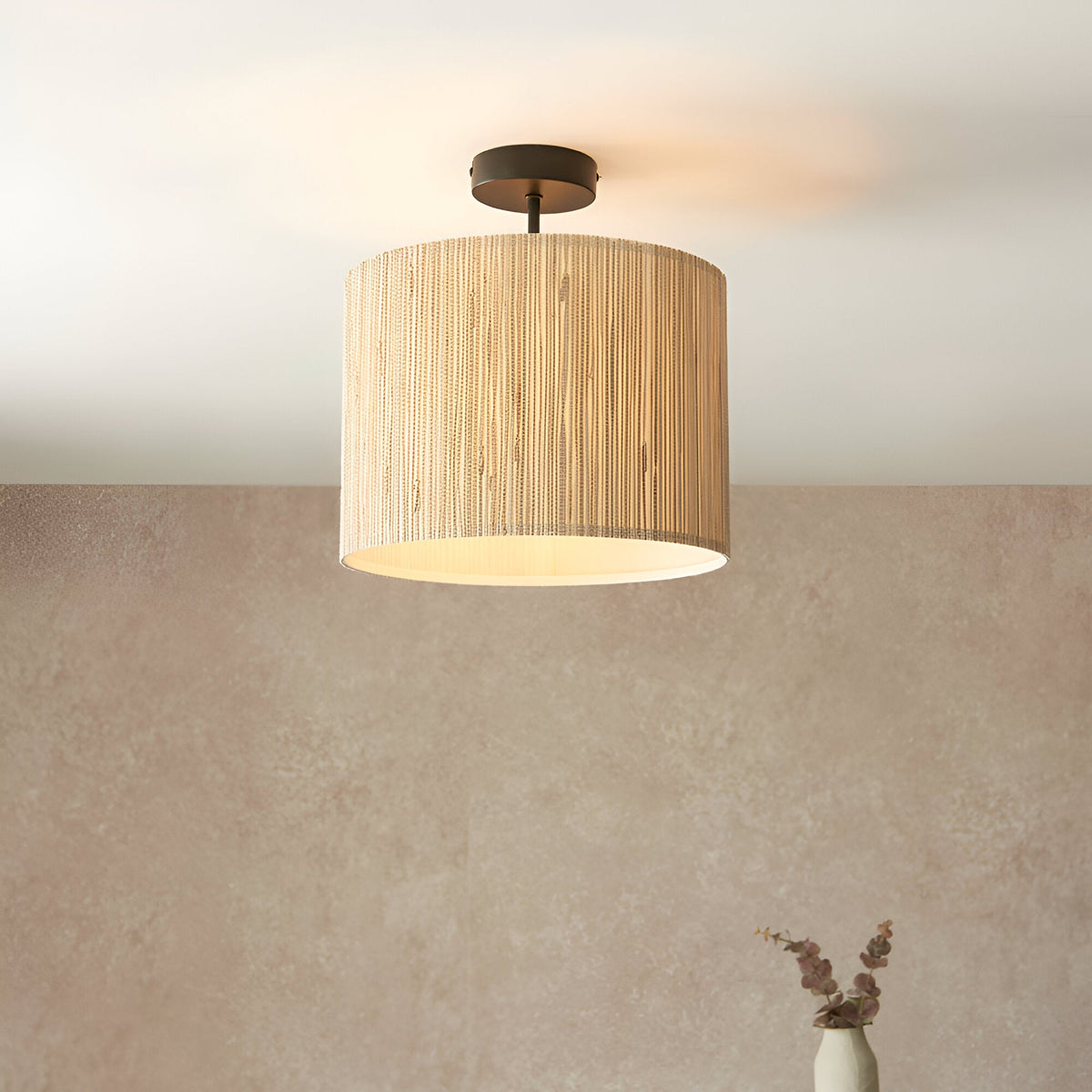 Endon Salcombe semi-flush ceiling light with woven seagrass drum shade and matt black fitting, installed on a ceiling above a warm-toned plaster wall.