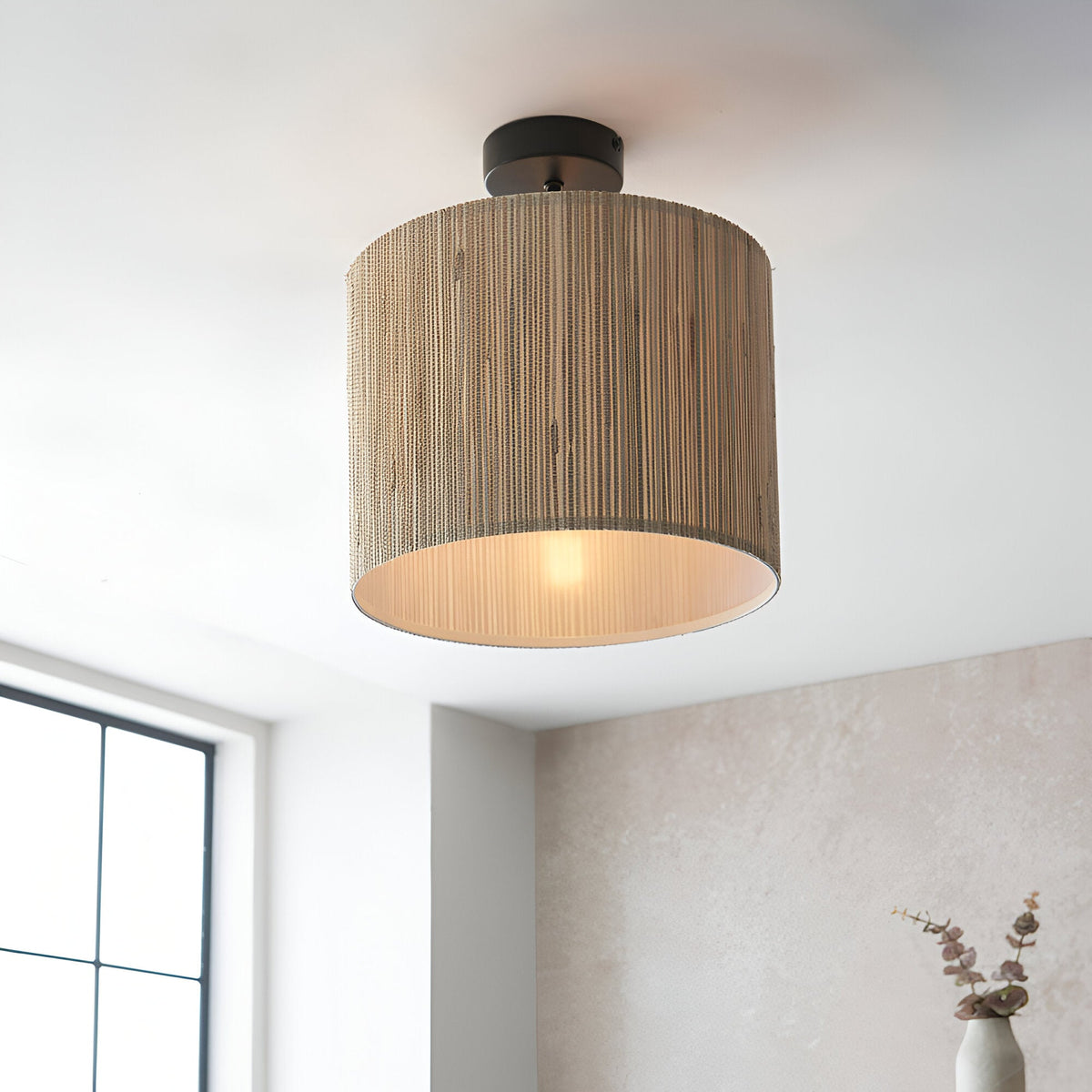 Endon Salcombe semi-flush ceiling light with woven seagrass drum shade and matt black fitting, illuminated on a white ceiling beside a window.
