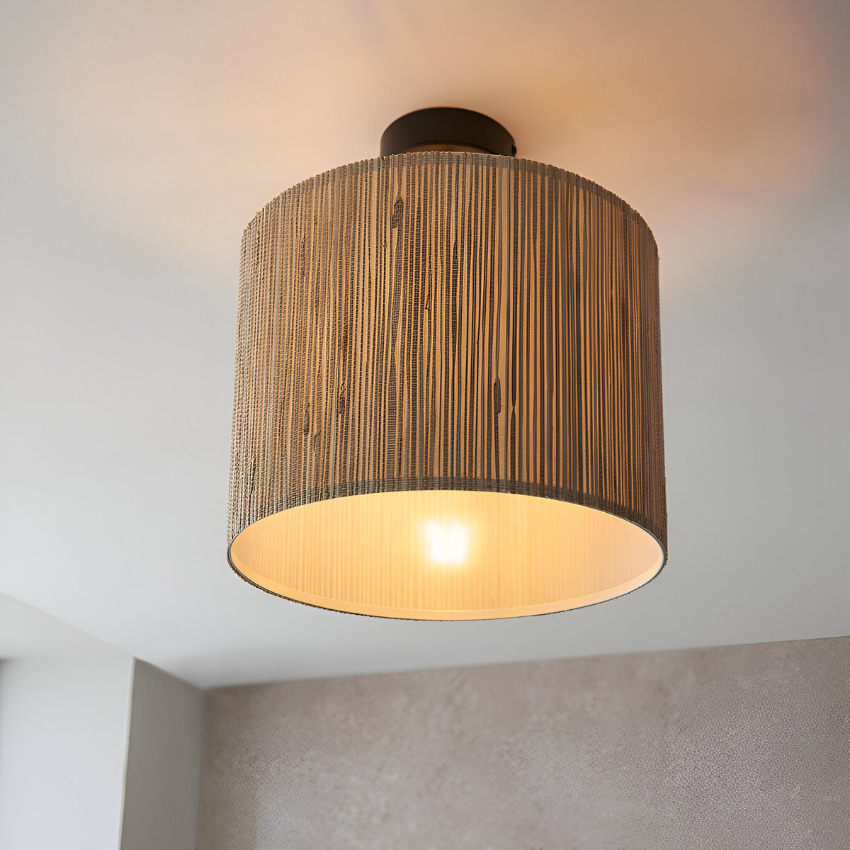 Endon Salcombe semi-flush ceiling light with a woven seagrass drum shade and matt black fitting, illuminated by a single E27 lamp against a white ceiling.