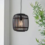 Bracken Pendant Light in black bamboo cage design with visible E27 filament bulb, hanging from black flex against a light wall near a green plant.
