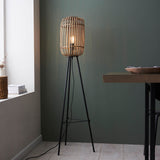 Bracken Floor Lamp in black and natural, with a bamboo cage shade on a matt black tripod base, shown lit in a living room setting.