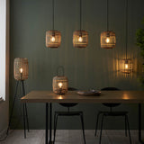 Bracken Floor Lamp with natural bamboo cage shade on black tripod base, shown in dining room with matching bamboo pendant lights above wooden table.