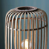 Bracken Floor Lamp close-up showing natural bamboo cage frame with dark wooden top ring and lit E27 bulb visible inside.
